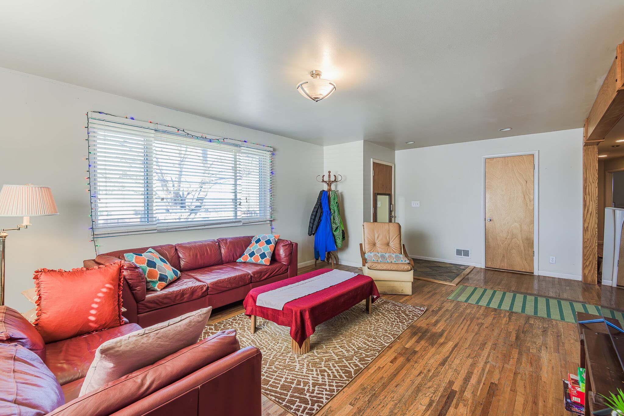 A living room with a red sofa, a bench, a chair, and a window with blinds.