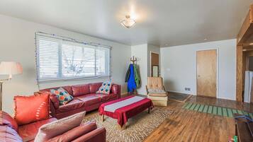 A living room with a red sofa, a bench, a chair, and a window with blinds.
