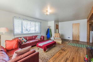 Ein Wohnzimmer mit einem roten Sofa, einer Bank, einem Sessel und einem Fenster mit Jalousien.