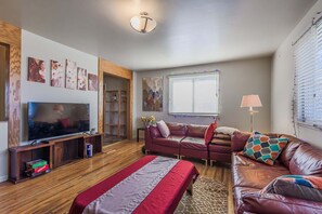 A living room with a TV, leather sofa, and a bed.