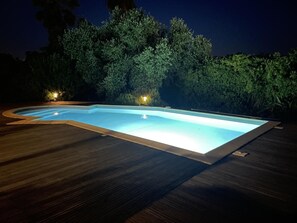 A swimming pool with a wooden deck, surrounded by dense foliage and illuminated by ambient lighting. - Villa Maddalena - BORGO (BORGO)