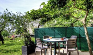 Un patio con una mesa redonda y cuatro sillas, rodeado de follaje y una cerca verde.