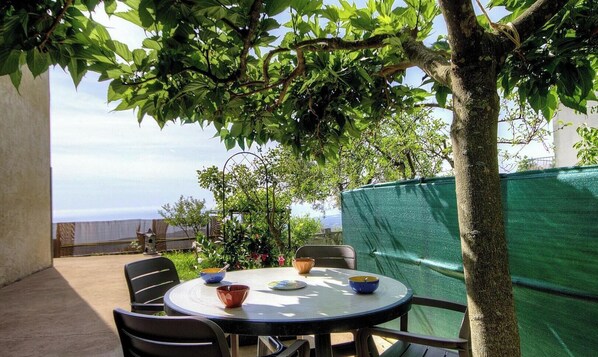 Un patio al aire libre con una mesa redonda, sillas y vista al mar.