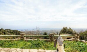Una estructura de piedra con un molino, un banco de piedra y vistas del paisaje.