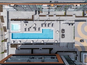 A rooftop pool area with seating, a small pool, and a modern building in the background. - Lake Days & Poolside Nights (Kelowna)