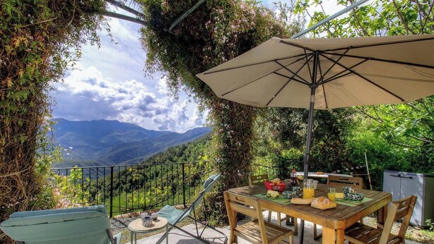 Un patio con mesa, sillas y sombrilla, con vistas a un paisaje montañoso.