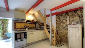 Une cuisine avec un escalier en bois, un mur en pierre et une vue sur l’extérieur.