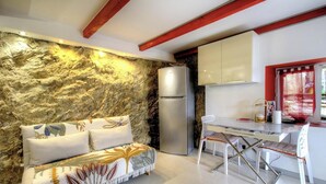 Una cocina moderna con pared de piedra, un refrigerador, una mesa de comedor con sillas y un sofá con cojines estampados.