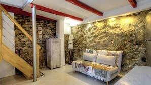 Una habitación con pared de piedra, escalera de madera, un sofá y una lámpara.