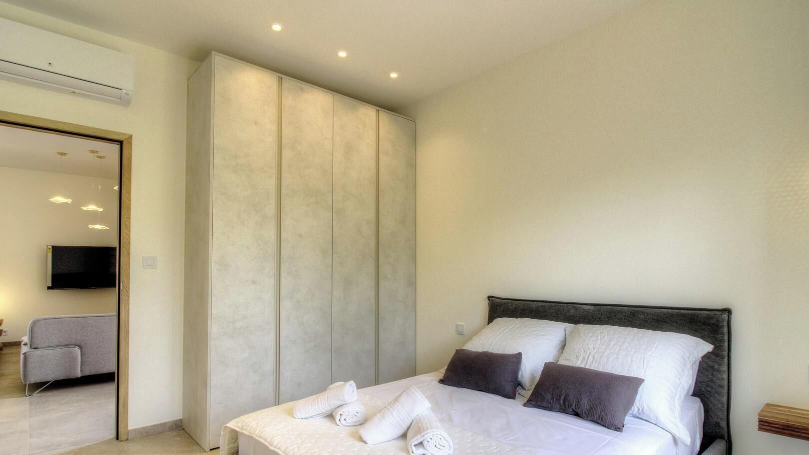A modern bedroom with a bed, pillows, a TV, and a sofa.