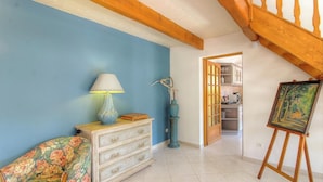 A room with a wooden staircase, a painting on an easel, a dresser with drawers, a lamp, and a vase with dried plants. - A Parniccia - PORTO VECCHIO (PORTO VECCHIO)