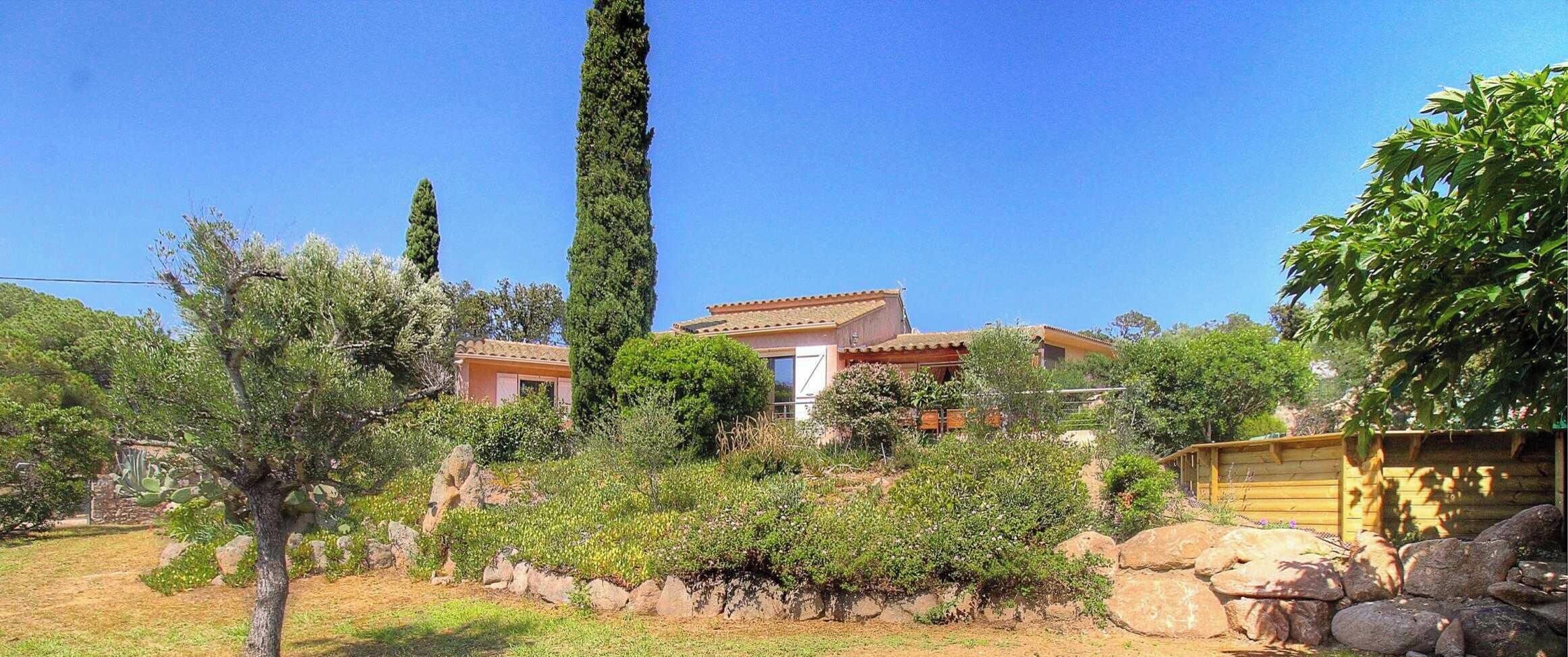 Eine mediterrane Villa mit Ziegeldach, umgeben von üppiger Vegetation und einer Steinmauer.