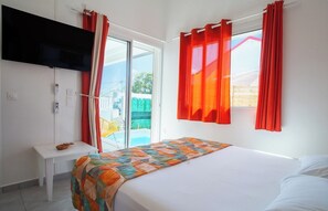 Ein Schlafzimmer mit einem Bett, einem an der Wand montierten Fernseher, einem kleinen Tisch und einem Fenster mit Vorhängen.