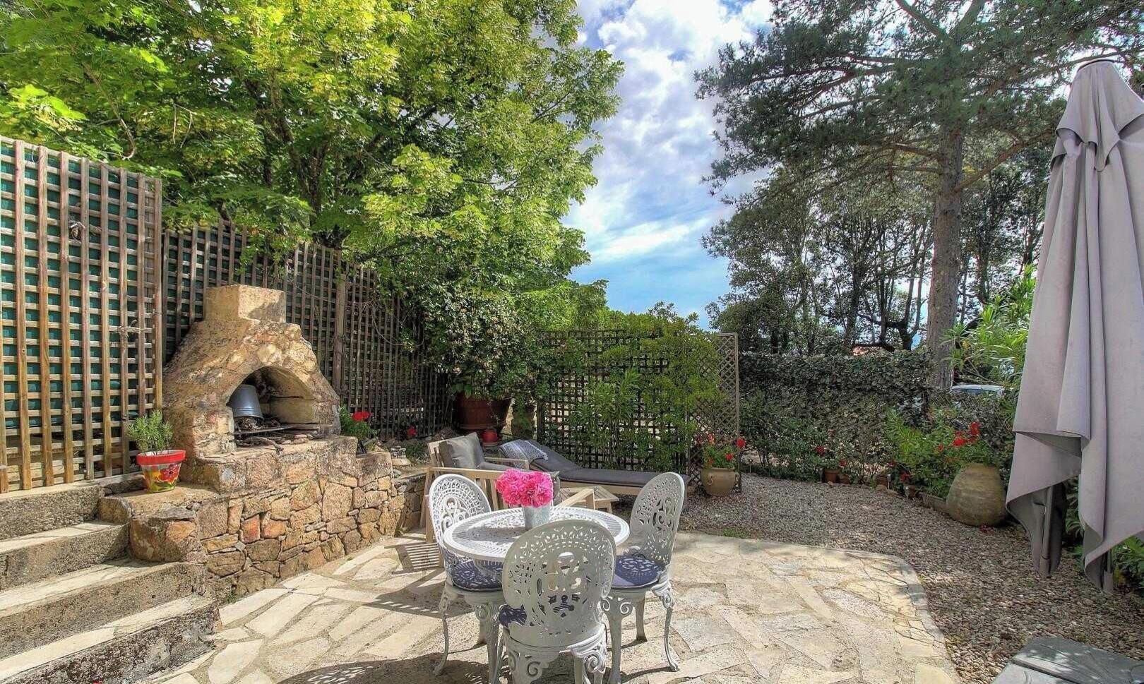 Een terras buiten met stenen trappen, een stenen haardvuur en een tafel met stoelen.