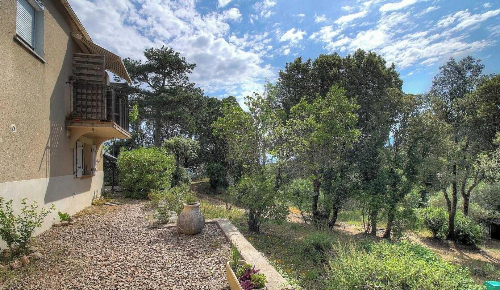 Et hus med balkon, omgivet af træer og en grussti.