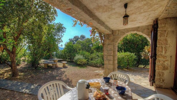 Un patio al aire libre con una mesa lista para comer, rodeado de muros de piedra y follaje.
