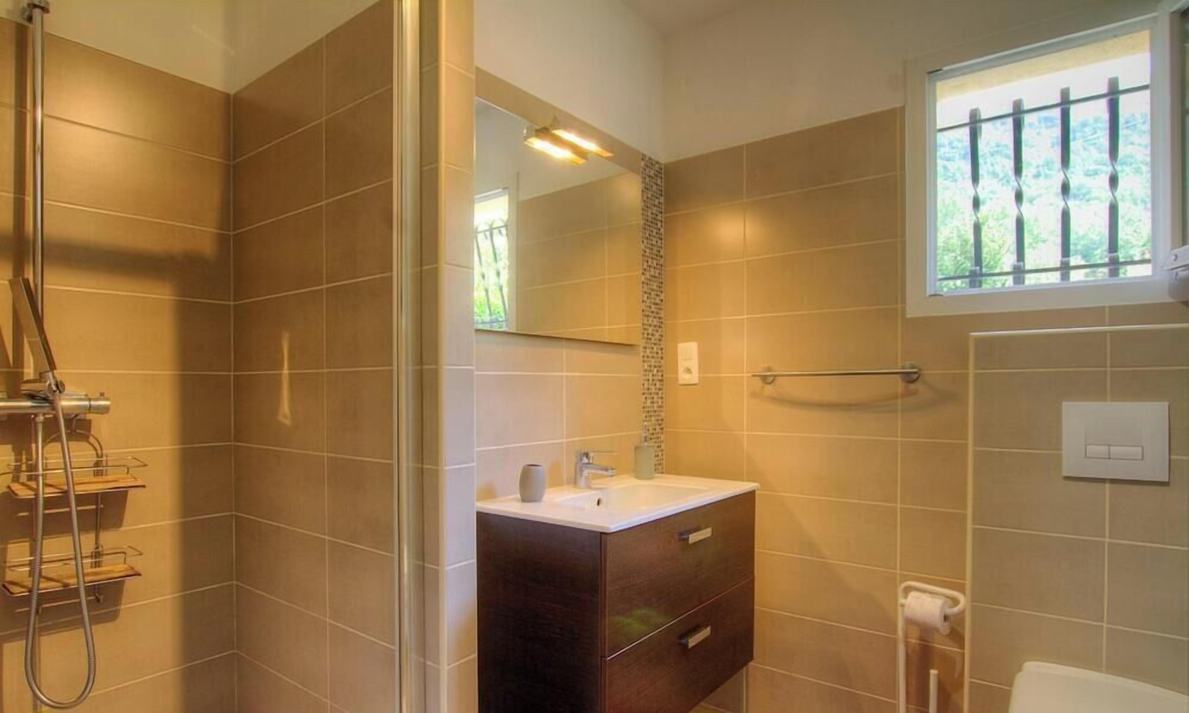 Une salle de bain avec une douche, un lavabo, un miroir et une fenêtre.