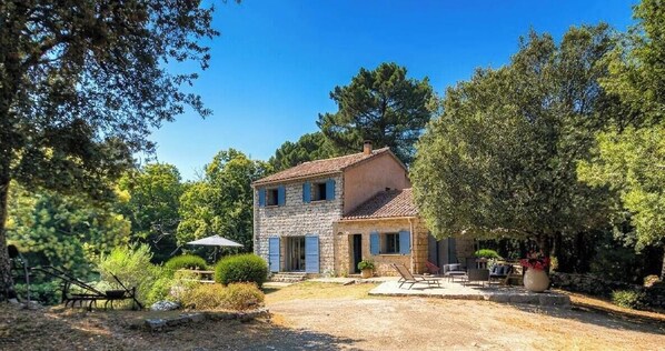 Kivitalo, jonka päällä on tiilikatto, ja sen ympärillä on puita sekä sorapäällysteinen ajotie.