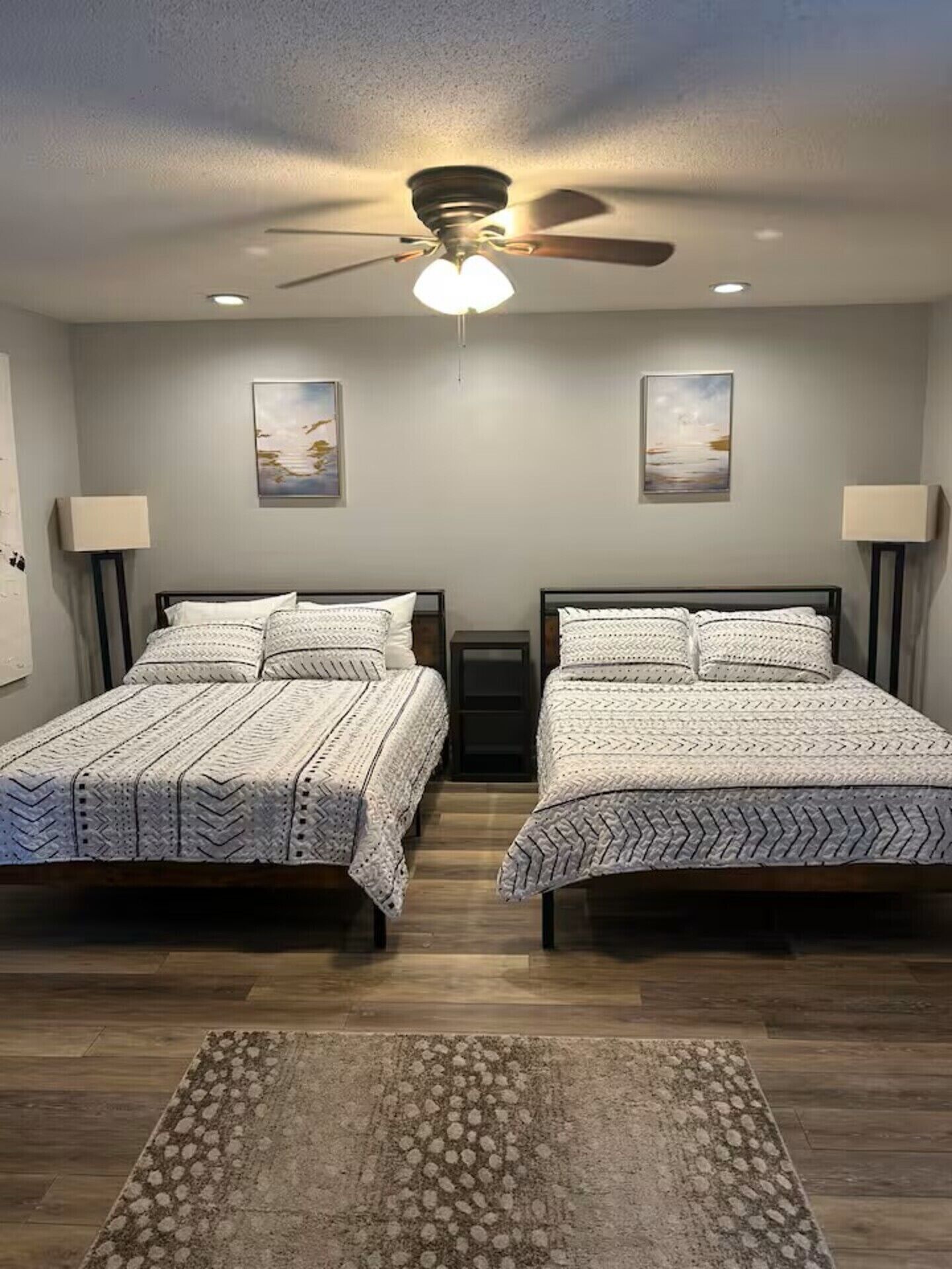 A room with two beds, a ceiling fan, and two wall-mounted lamps.