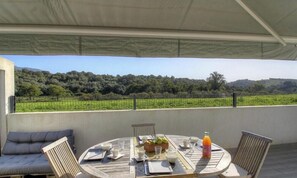 Un'area pranzo all'aperto coperta con un tavolo apparecchiato per quattro, affacciata su una vigna.