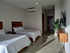 A hotel room with two beds, a wooden headboard, a wall-mounted air conditioner, a wooden nightstand, a TV, and a plant.