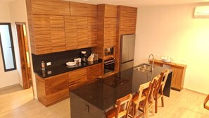 Una cocina moderna con armarios de madera, encimera negra, refrigerador de acero inoxidable y un comedor con sillas de madera.