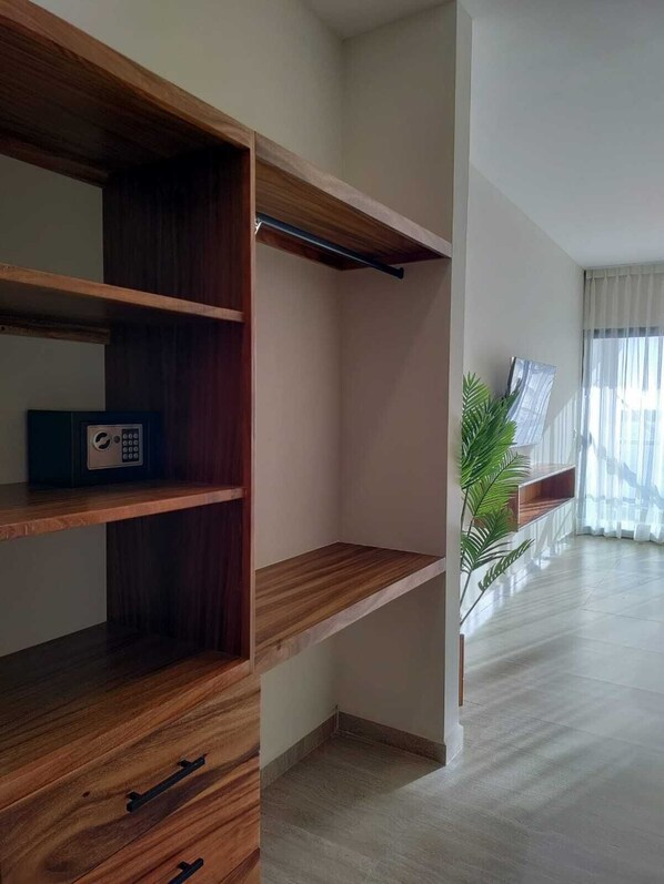 Una habitación moderna con estanterías de madera integradas, una planta pequeña y un ventanal con cortinas de gasa.