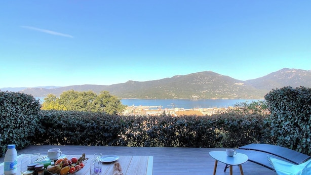 Eine Terrasse mit Esstisch, einem Stuhl und Blick auf einen See und Berge.