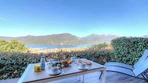 Ein Tisch ist mit Frühstücksleckereien gedeckt und bietet Blick auf einen See und Berge.