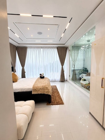 A modern bedroom with a large bed, a sofa, a glass shower, and a wardrobe.