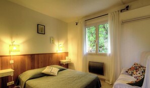 A hotel room with a bed, bedside lamps, a window with curtains, a radiator, and a chair with a floral pillow. - Ortu di Casa - MURATO (MURATO)