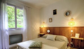 Ein Schlafzimmer mit einem Bett, zwei Nachttischlampen, einem Fenster mit Vorhängen, einer Heizung und einem an der Wand befestigten Regal mit einem Bild.