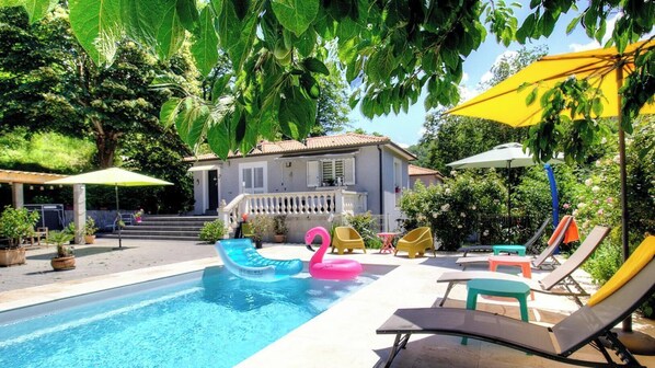 A swimming pool with inflatable toys, outdoor seating, and a house in the background. - U Castellu di Garanza (SAN DAMIANO)
