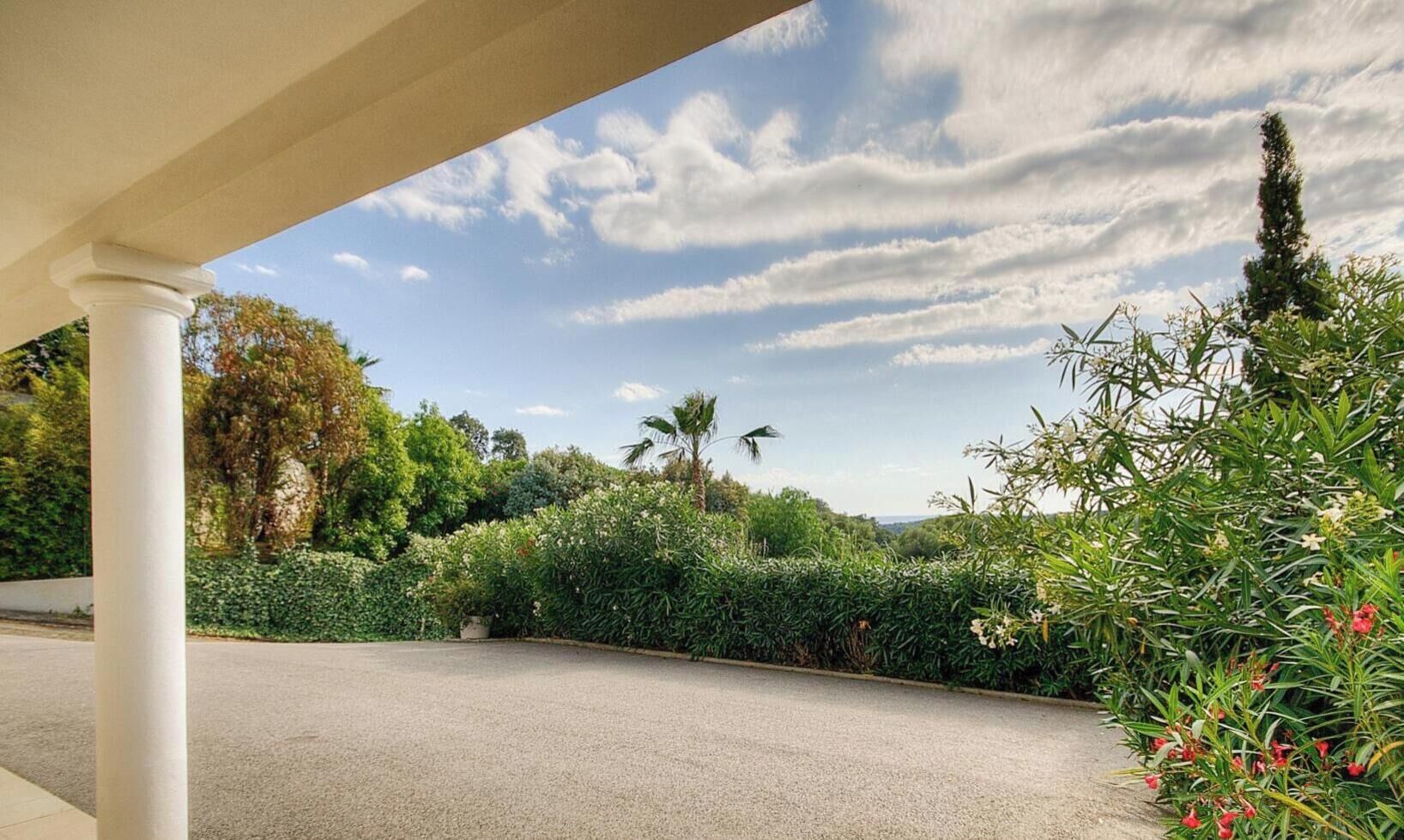Un'area di parcheggio coperta con vista su un giardino curato e un cielo sereno.