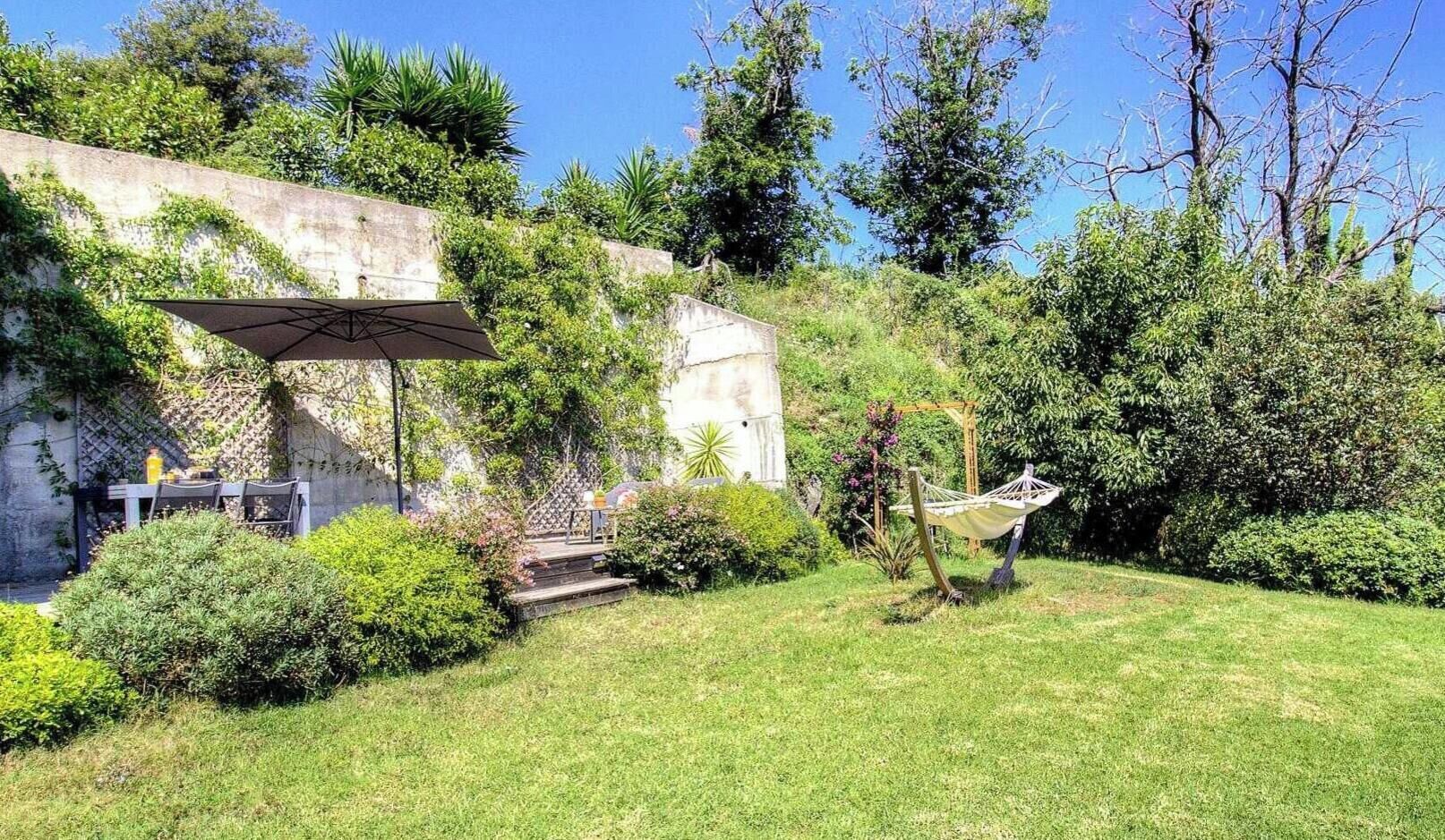 A garden with a hammock, a table with chairs, and a pergola.