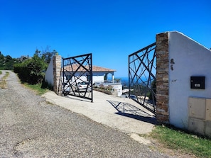 Ein verschlossenes Tor führt zu einem Anwesen mit einer Steinmauer und einem Metallgitter, einer gepflasterten Auffahrt und einem Gebäude mit einem Ziegeldach im Hintergrund.