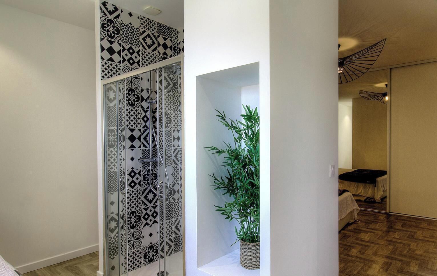 Une pièce avec un mur orné de motifs, une plante en pot, un lit et un ventilateur de plafond.
