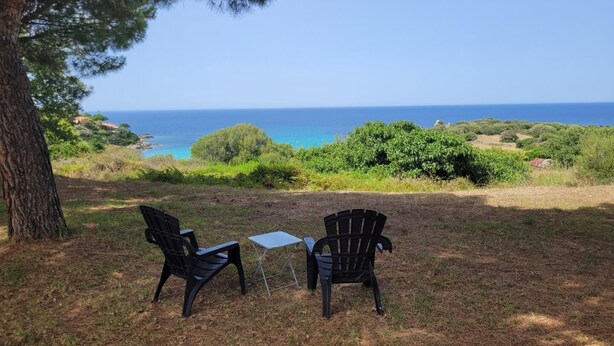 Deux fauteuils Adirondack, une petite table en métal et une vue sur l’océan.