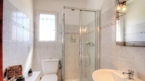 Un bagno con doccia vetrata, un water, un lavandino e una finestra che lascia entrare luce naturale.