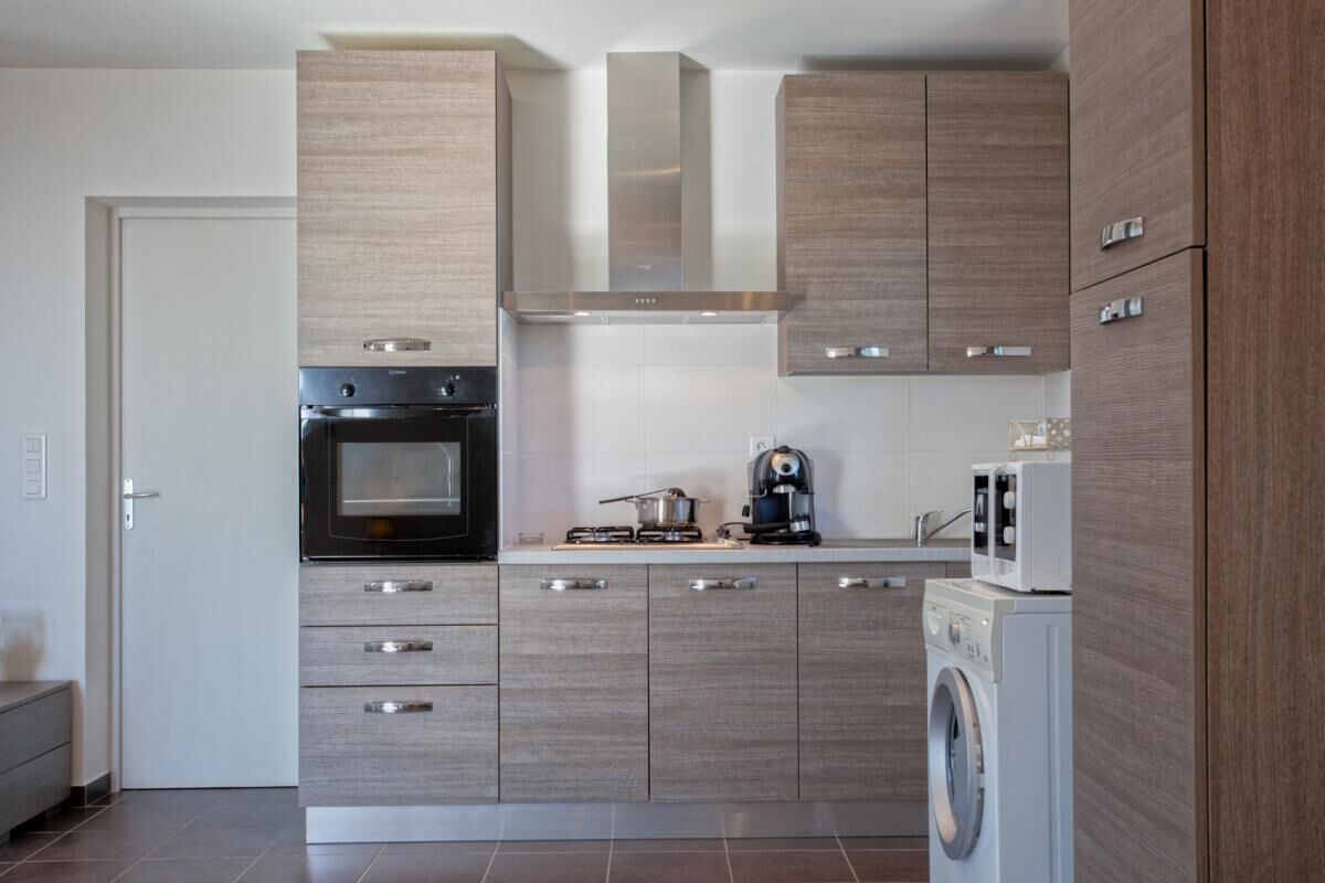 A modern kitchen with built-in appliances, wooden cabinets, and a washing machine.