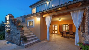 Ein Haus mit einer Steintreppe, einem Essbereich mit Tisch und Stühlen sowie einer überdachten Terrasse.