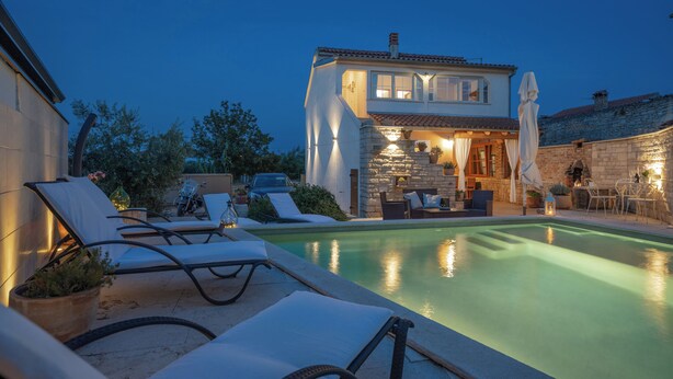 Ein zweistöckiges Haus mit Swimmingpool, Liegestühlen und einer Steinmauer.