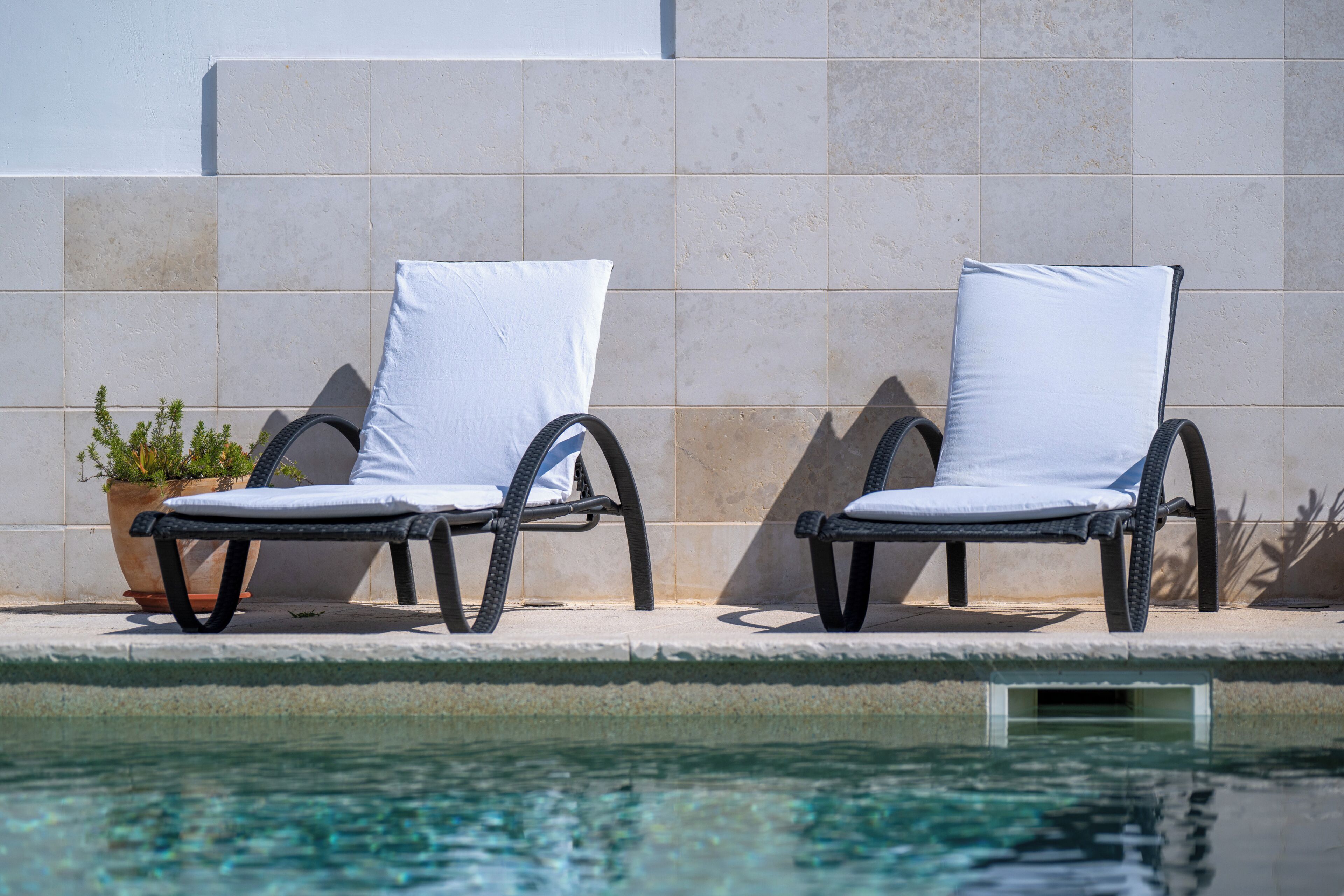 Deux fauteuils de relaxation avec des coussins blancs, placés près d’une piscine.