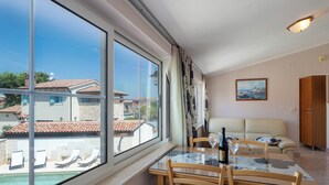 Ein Zimmer mit Glastisch, Stühlen, einer Couch, einem Gemälde und Blick auf einen Swimmingpool und Gebäude.