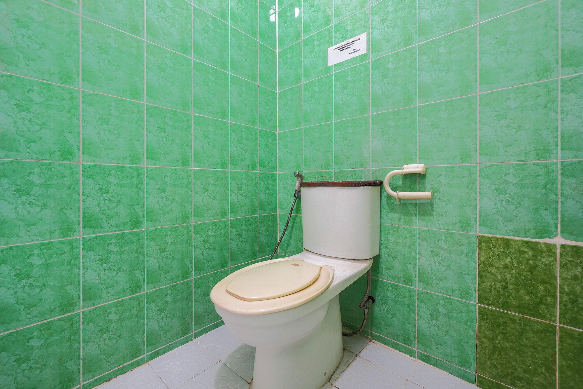 Un bany amb rajoles verdes, un vàter i una dutxera.
