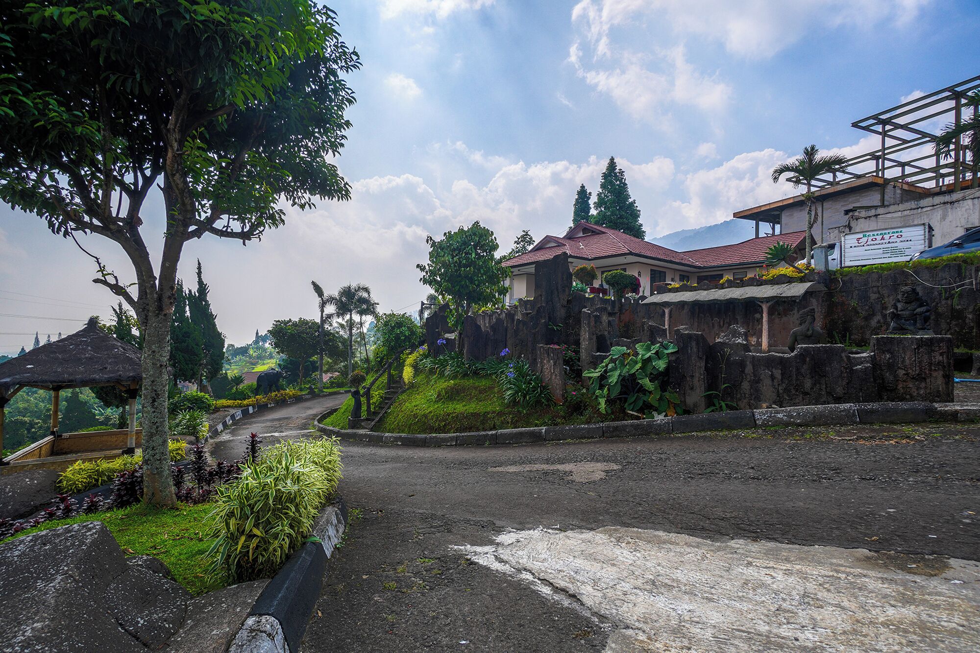 A paved pathway leading to a building with a red roof, surrounded by greenery and trees.