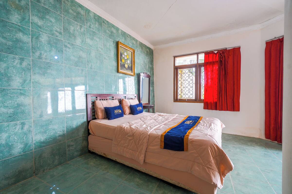 Un dormitorio con una cama, una ventana con cortinas rojas y un cuadro en la pared.