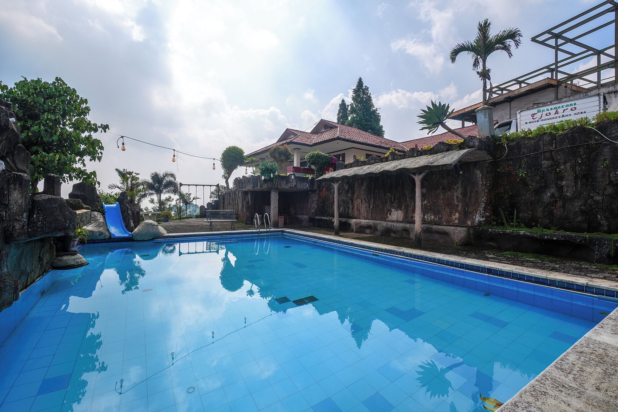 A swimming pool with a slide, surrounded by stone walls and tropical plants.