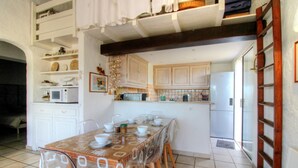 Zona pranzo con tavolo apparecchiato per quattro, cucina con pensili in legno chiaro e frigorifero bianco.