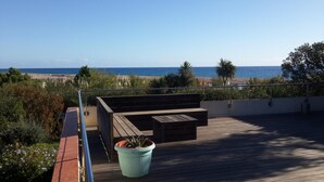 Un pontile in legno con una panca integrata e una pianta in vaso, con vista sulla spiaggia e sull'oceano.